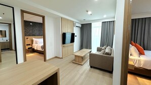 A modern hotel room with a wooden floor, a flat-screen TV, a sofa, a bed with orange pillows, and a large mirror. - Howard Johnson By Wyndham Tangerang (Tangerang)