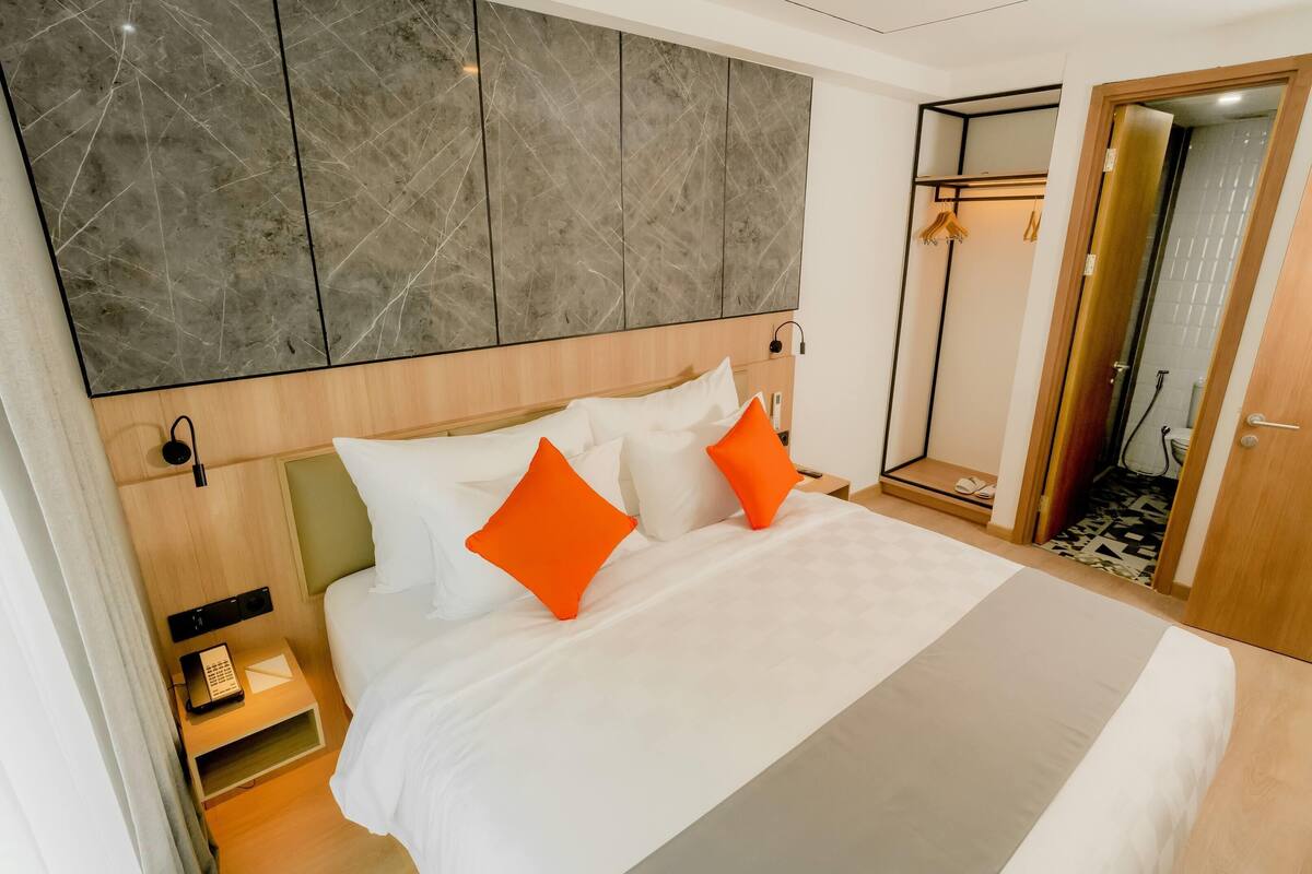 Una habitación de hotel con una cama grande, cabecera de madera, pared de mármol, armario y zona de ducha.