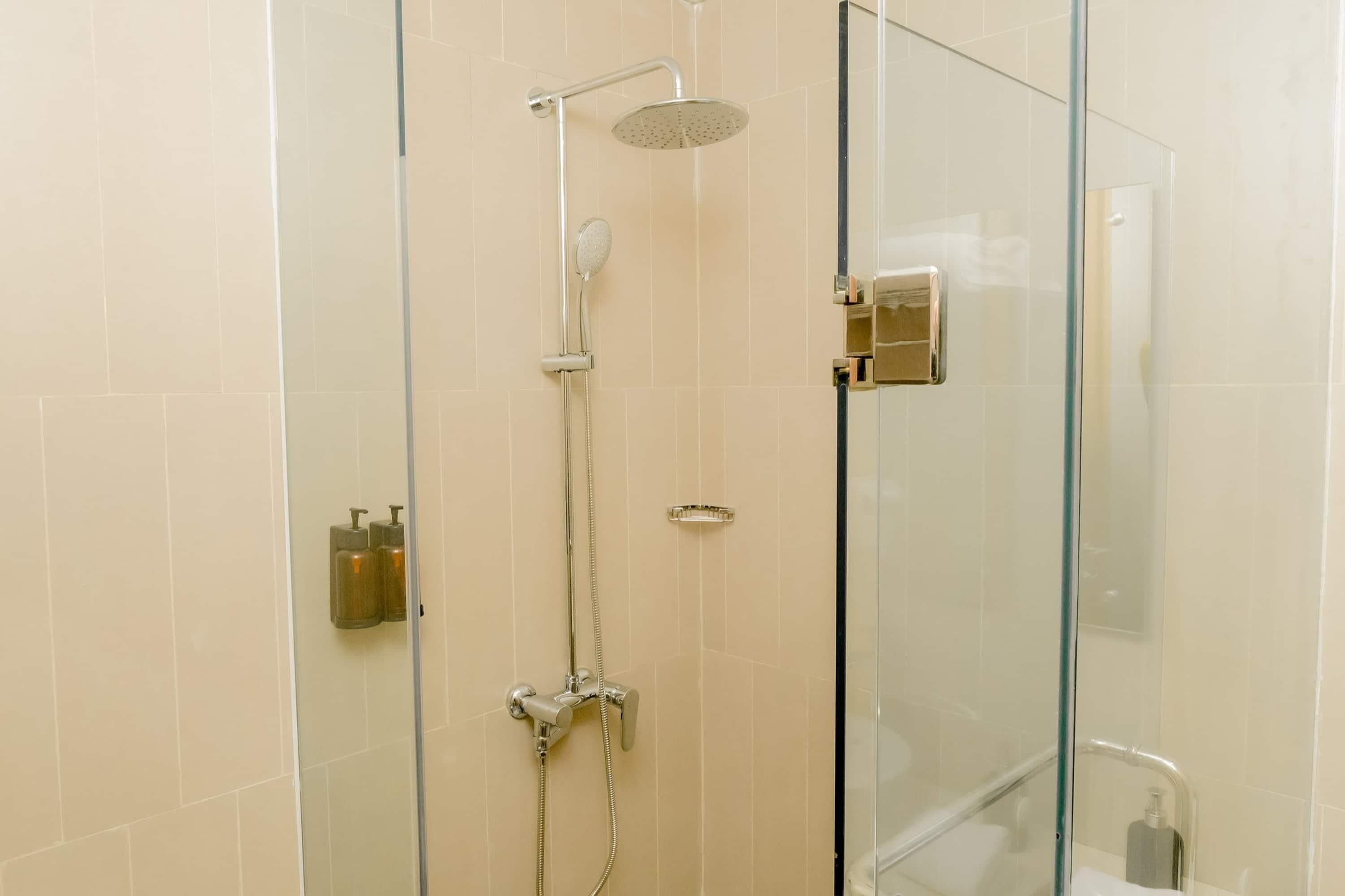 A glass-enclosed shower with a handheld showerhead and a wall-mounted faucet.