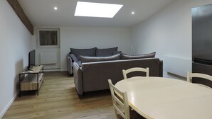 A compact living space with a sofa, a dining table, and a TV. - townhouse (saujon)