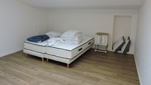 A small, bright room with a skylight, a bed with white bedding, a small wooden cabinet, and a door. - townhouse (saujon)