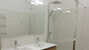 A modern bathroom with two sinks, a large mirror, and a glass shower enclosure. - townhouse (saujon)