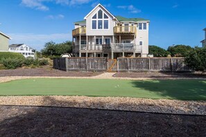 A two-story house with a balcony, a green lawn, and a wooden fence. - Sandy Pants-Walk to Beach! (Duck)