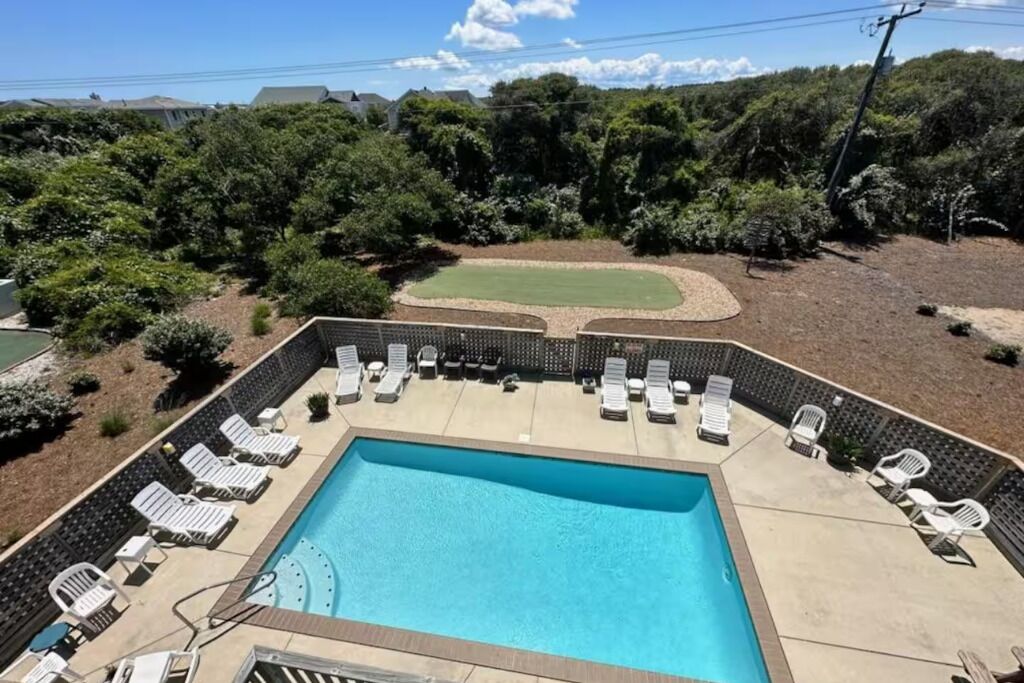 A rectangular swimming pool with lounge chairs and a small lawn area.