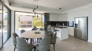 A modern kitchen with a central island, stainless steel appliances, and a dining area with a round table and chairs. - Noble Opatija Riviera Villa Mila (Veprinac)