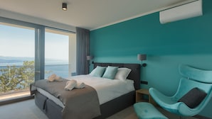 A modern hotel room with a large bed, a teal accent wall, a view of the outdoors, and a unique teal chair. - Noble Opatija Riviera Villa Mila (Veprinac)