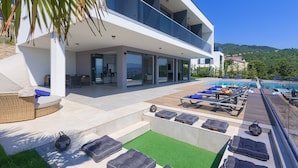 A modern outdoor pool area with lounge chairs, a seating area, and a view of a mountain. - Noble Opatija Riviera Villa Mila (Veprinac)