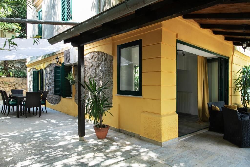 A yellow building with a stone facade, green shutters, and outdoor seating.
