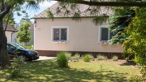 Una casa de dos pisos con fachada color beige, marcos de ventanas blancos y un pequeño jardín con un automóvil estacionado frente a ella.