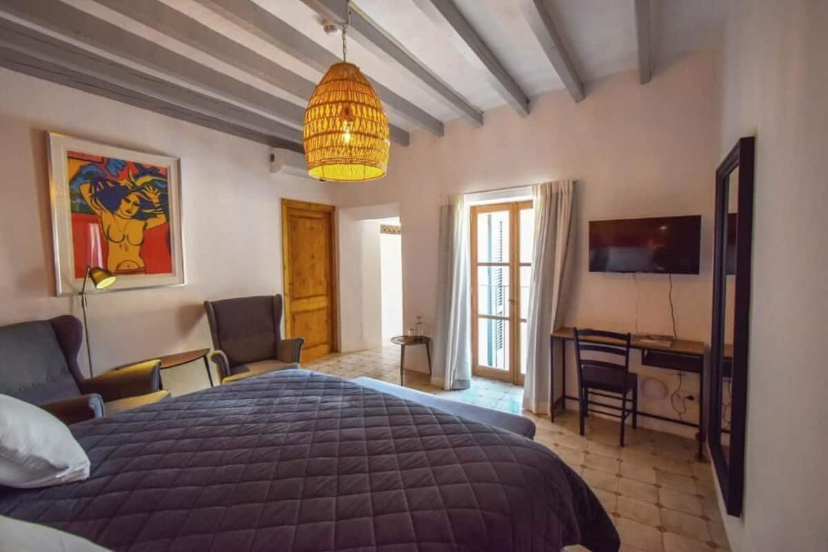 A bedroom with a large bed, a desk, a chair, a television, and a painting on the wall.