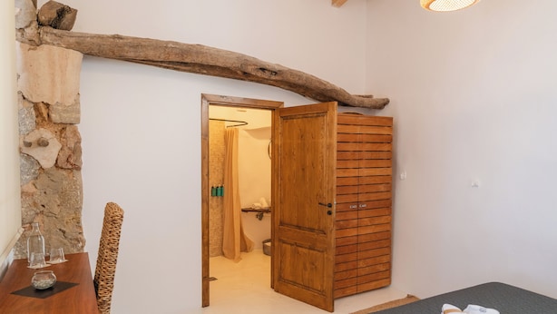 A room with a bed, a wooden door, a stone wall, and a table with glasses and a menu. - Solleric Petit Hotel (Sóller)