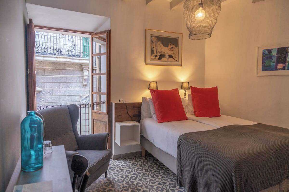 A hotel room with a bed, two bedside tables, a chair, a small table with a blue bottle, and a patterned floor.