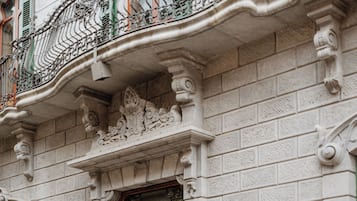 Fachada de edificio con detalles arquitectónicos ornamentales, incluyendo un acceso decorativo y un balcón con barandillas de hierro forjado.