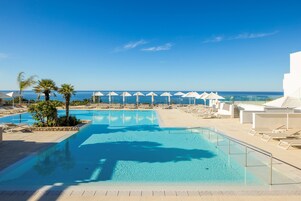 Una piscina con sillones de descanso y sombrillas, cielo despejado y vista al mar.