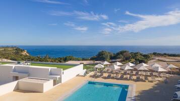 Una piscina con vista al mar, sillas de descanso y sombrillas.
