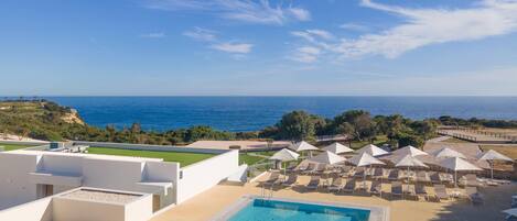 Una piscina con vista al mar, sillas de descanso y sombrillas.