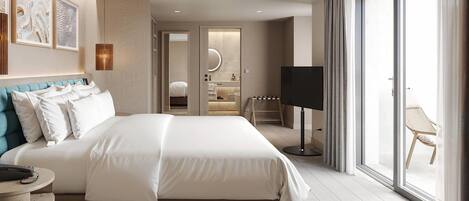 A modern hotel room with a large bed, a desk, a TV, and a sliding glass door to a balcony.