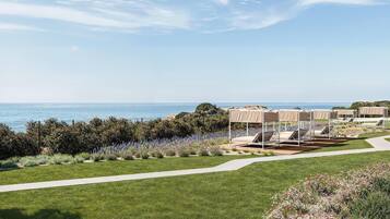 A coastal hotel with outdoor seating areas, a pathway, and a view of the sea.