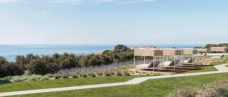 A coastal hotel with outdoor seating areas, a pathway, and a view of the sea.