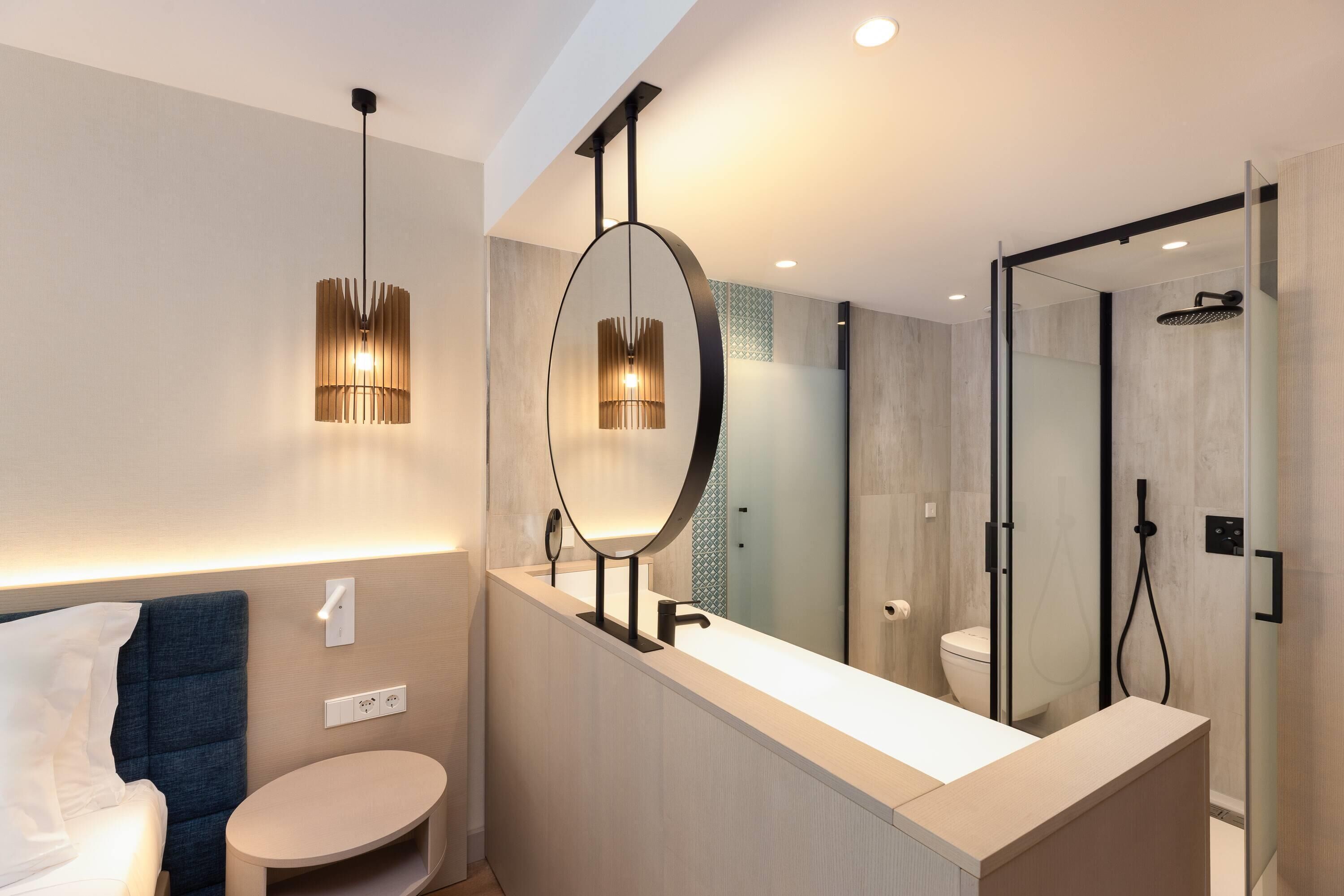 Un bagno moderno con uno specchio grande, un mobiletto dal design rotondo, un box doccia e un letto con testiera blu.