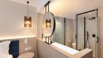 Une salle de bain moderne avec un grand miroir, un meuble-lavabo rond, une cabine de douche et un lit doté d’une tête de lit bleue.