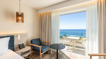 Una habitación de hotel con una cama, un escritorio con teléfono, una silla, una mesa redonda y un balcón con vistas al océano.