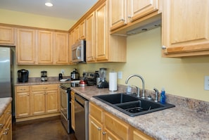 A kitchen with wooden cabinets, a stainless steel refrigerator, a microwave, a stove, and a sink.