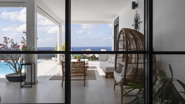 Een moderne woonkamer met uitzicht op de oceaan, een groot raam en een rieten stoel.