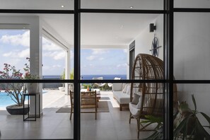 Una sala de estar moderna con vista al océano, un ventanal grande y una silla de mimbre.
