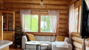 En stuga med träpanel på insidan, inredd med en soffa, ett litet bord, en matta och en tv.