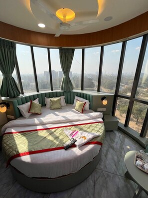 Une chambre d’hôtel située dans un immeuble de grande hauteur, avec un lit aux courbes élégantes, de grandes fenêtres et une vue sur la ville.