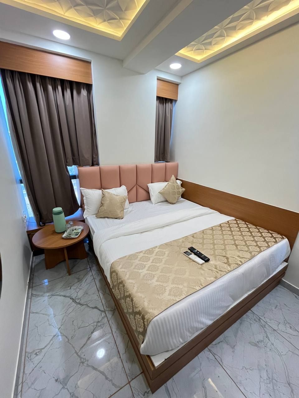 A hotel room with a large bed, a bedside table with a green water bottle, and a nightstand with a remote control.