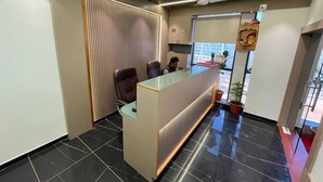 Un espace d’accueil avec un bureau en verre, un sol carrelé de carreaux noirs et un ventilateur de plafond.