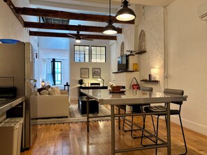 Una cocina moderna con vigas de madera, un comedor con mesa de vidrio y una sala de estar acogedora con sofá.