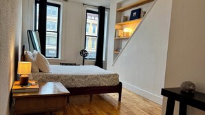 A compact bedroom with a bed, bedside table, lamp, and a small desk. - Modern Studio APT in the Heart of Downtown Geneva (Geneva)