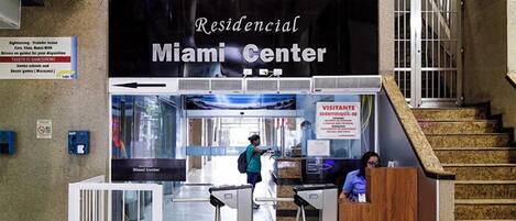 Zona de recepción en el Miami Center con un cartel que indica que es un alojamiento residencial. Se observan mostradores de recepción, una escalera y un punto de control de seguridad.