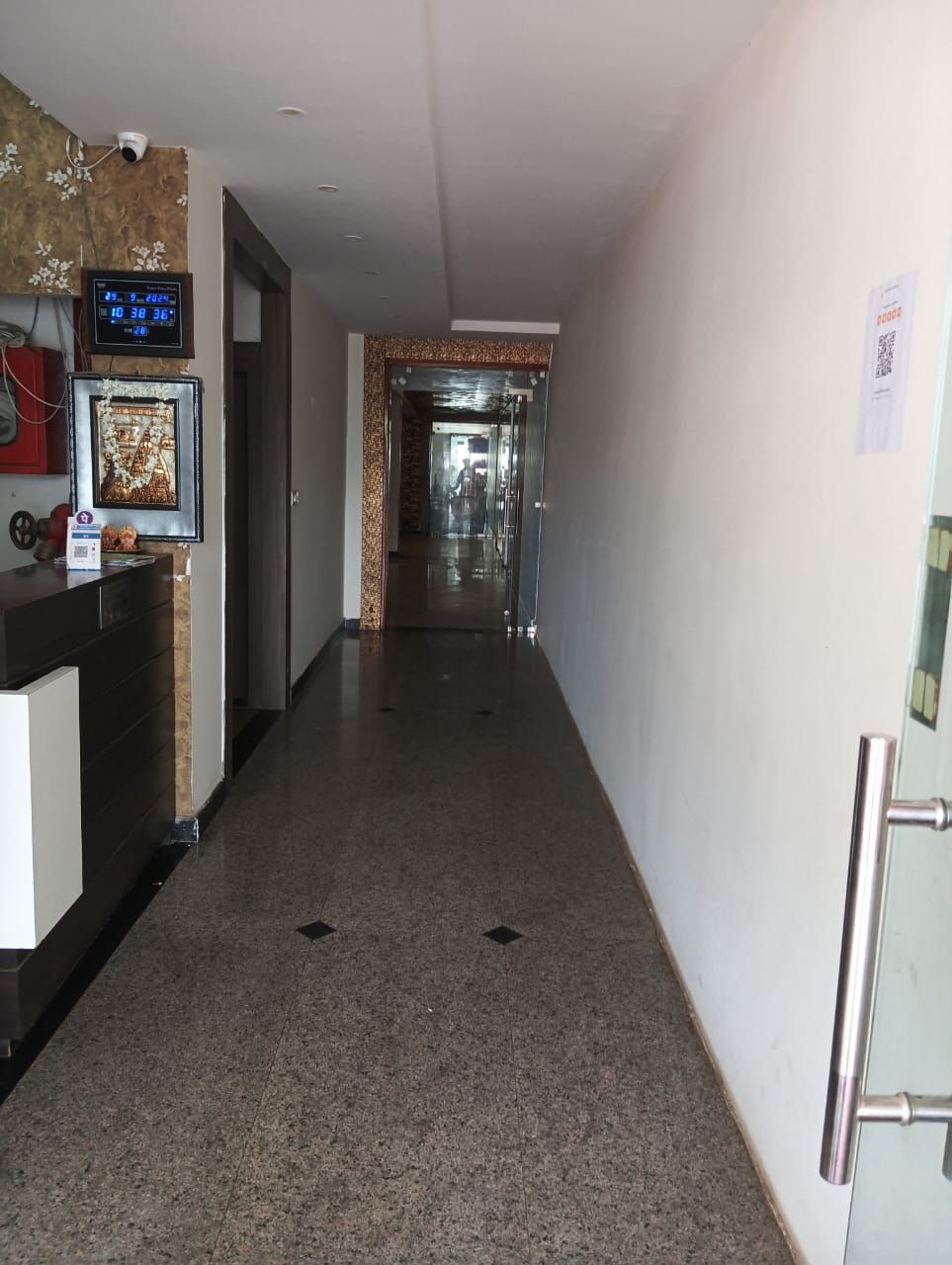 A hotel corridor with a reception desk, a digital clock, and a framed picture.