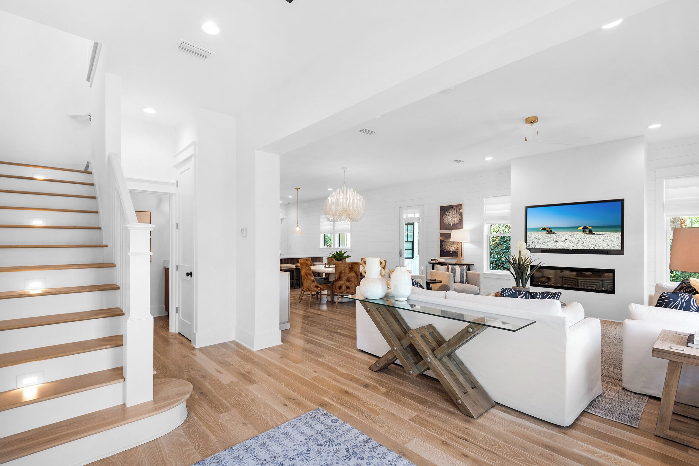 A modern living room with a glass coffee table, white sofas, and a TV mounted on the wall.