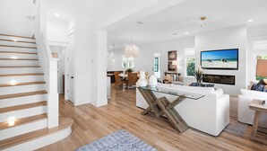 A modern living room with a glass coffee table, white sofas, and a TV mounted on the wall.