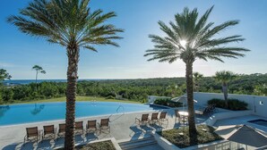 A pool area with lounge chairs and palm trees, overlooking a scenic landscape.