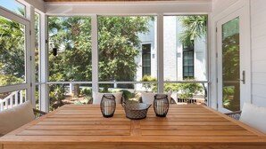 A wooden table with two black candle holders and a woven basket, set in a room with large windows and white walls.