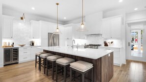 A modern kitchen with white cabinetry, a large island with bar stools, stainless steel appliances, and pendant lighting.