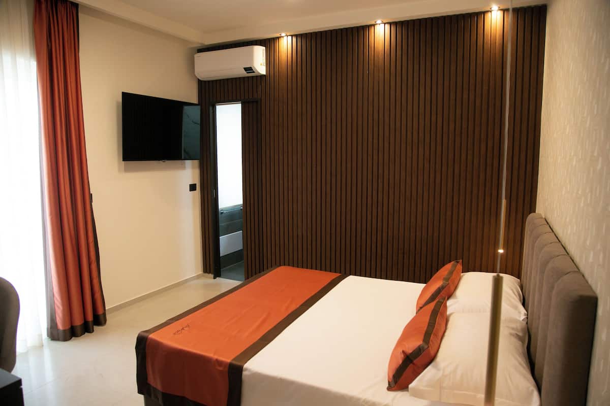 Quarto de hotel com cama, televisão de tela plana na parede e janela com cortinas.