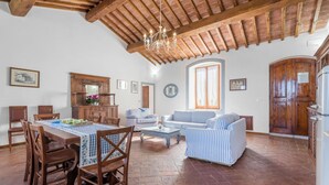 Un amplio salón con una mesa de comedor, sillas de madera, un sofá y una araña.