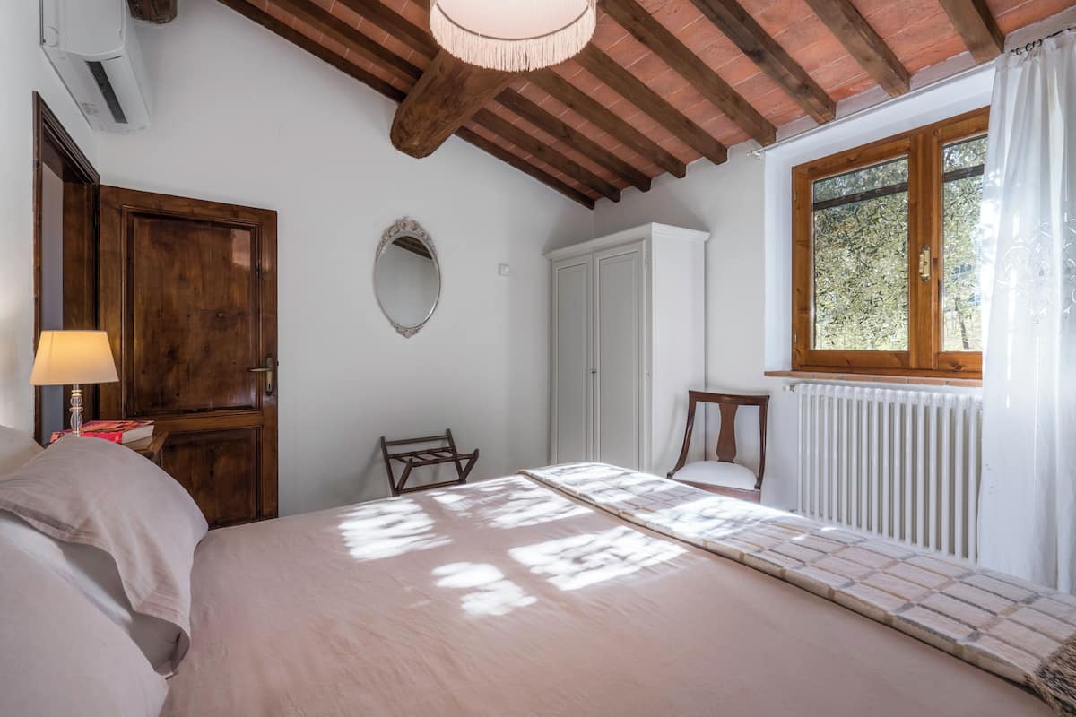 Un dormitorio con techo de madera, una cama, un ventanal con cortinas, un radiador y un armario.