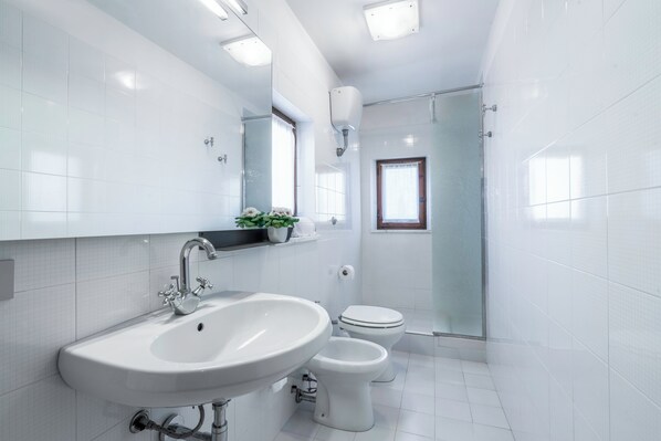 Un baño moderno con lavamanos, dos inodoros, ducha y ventana.