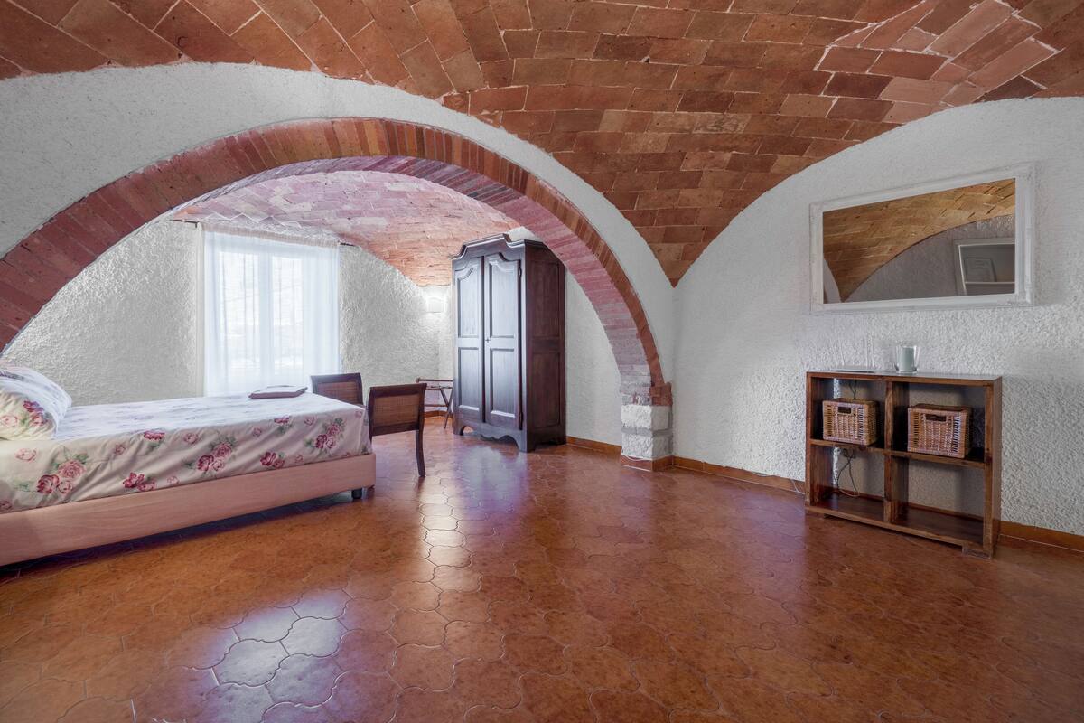 Un dormitorio con techo de ladrillo, una cama con edredón estampado de flores, un armario de madera y una ventana pequeña.