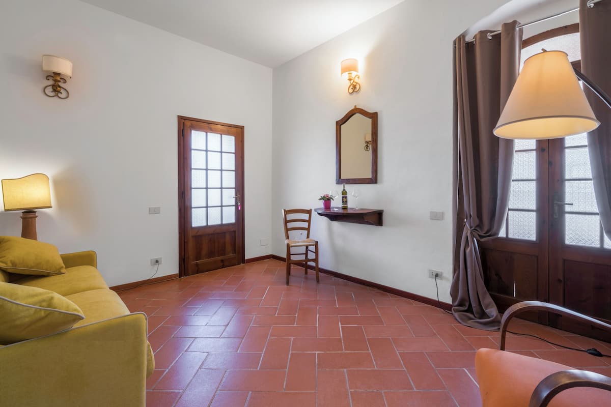 Una habitación con un sofá amarillo, una silla de madera, un espejo y una lámpara.
