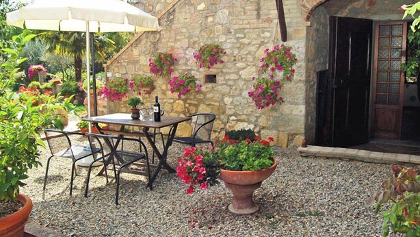 Un patio al aire libre con pared de piedra, mesa y sillas, y plantas en macetas.