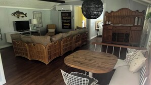 Un salon spacieux avec un grand canapé en forme de L, une table à manger et une chaise blanche. On y trouve également un meuble en bois et un poisson décoratif accroché au mur.